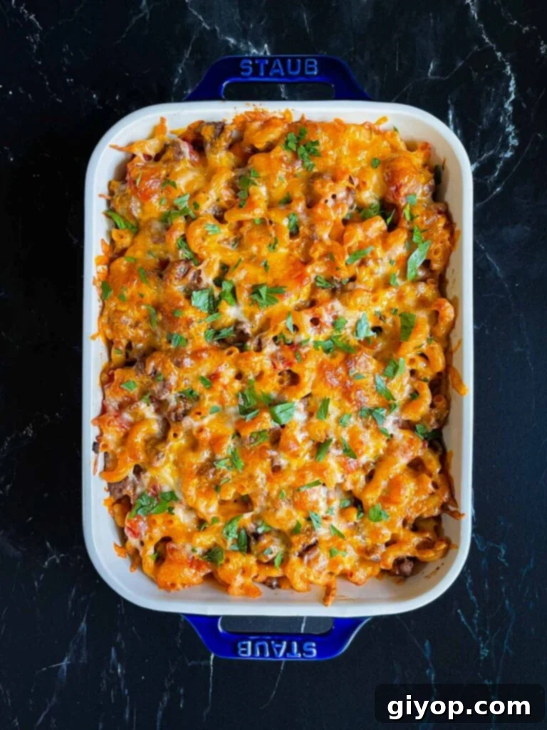 Comforting Homemade Cheesy Beefaroni 9 A baked Cheesy Beefaroni casserole in a blue dish, elegantly garnished with freshly chopped parsley.