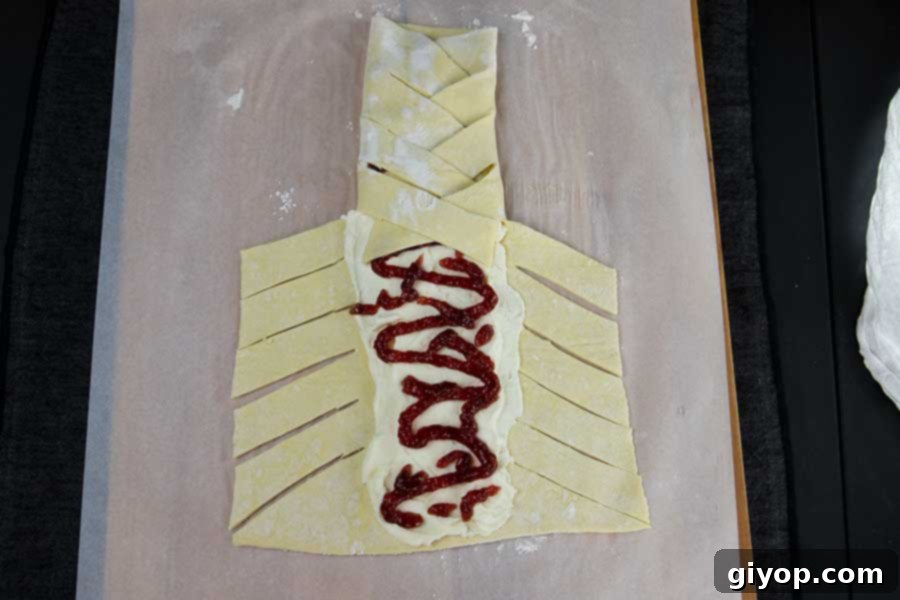 Raspberry Cream Cheese Swirl Danish 4 Raw puff pastry with the creamy cheese mixture spread down the middle, topped with vibrant raspberry jam, ready for braiding.