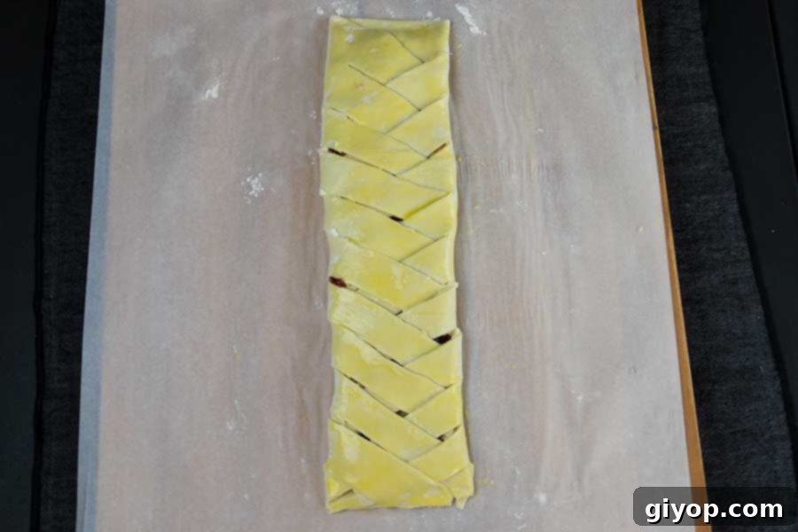 Raspberry Cream Cheese Swirl Danish 5 Puff pastry meticulously braided over the raspberry cream cheese filling, resting on parchment paper before baking.