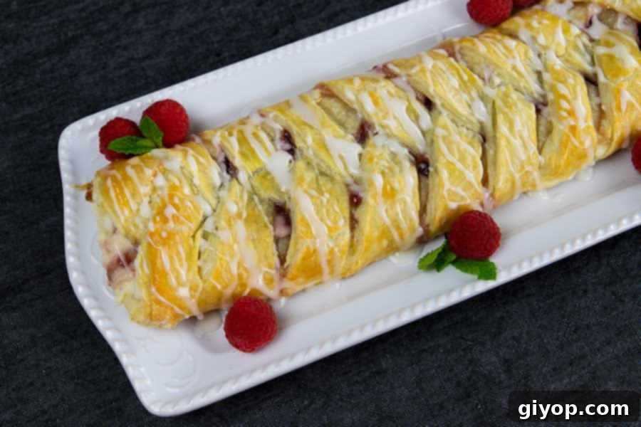 Raspberry Cream Cheese Swirl Danish 7 A glorious finished Raspberry Cream Cheese Danish, artfully garnished with fresh raspberries and mint, ready to be enjoyed on a white platter.