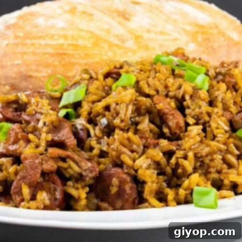 Cajun jambalaya in a white serving bowl with a loaf of bread in the background.