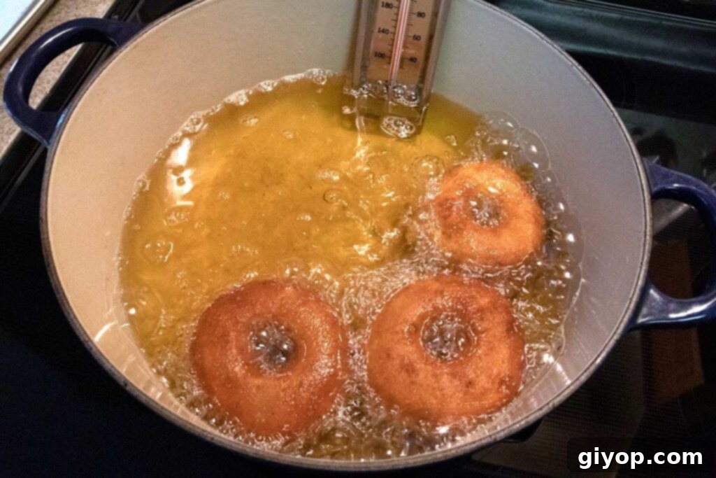 Ultimate Apple Cider Donuts Boiled Cider Edition 5 Golden-brown apple cider donuts frying in hot oil within a Dutch oven, surrounded by bubbling oil.