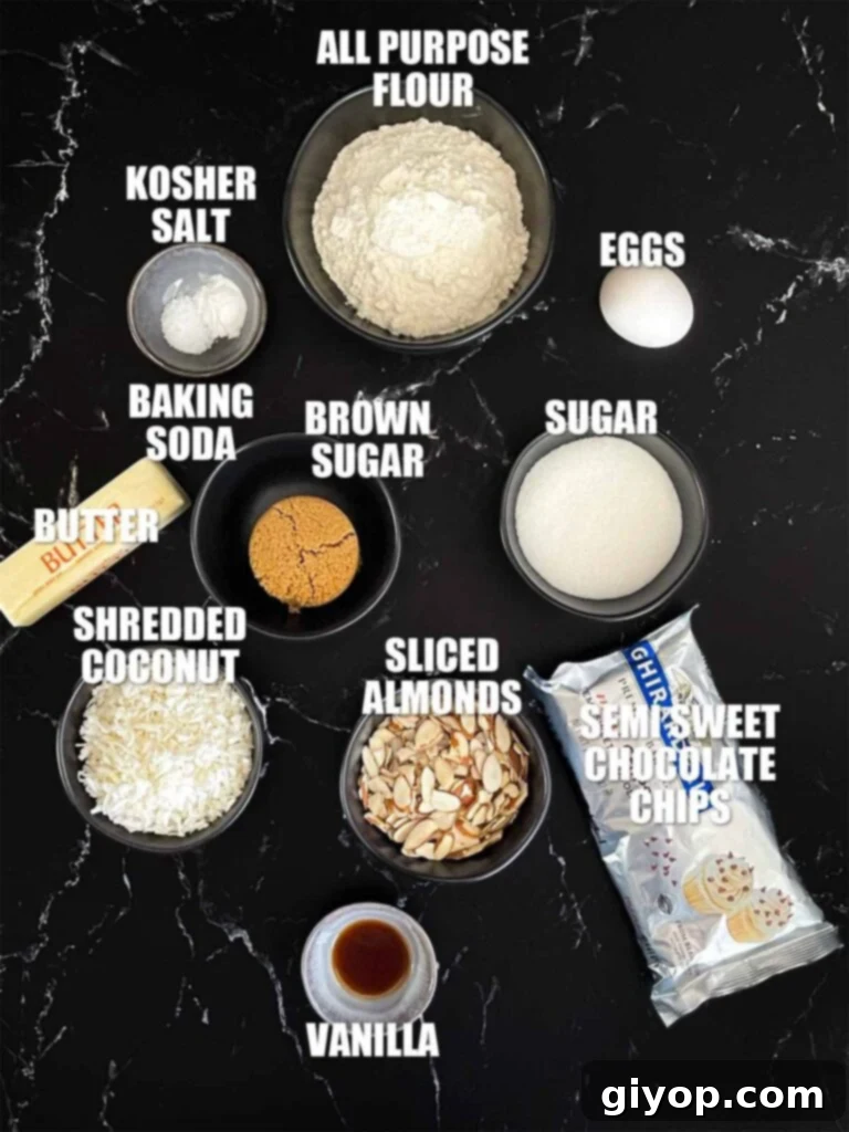 A curated display of ingredients for Almond Joy cookies on a dark rustic surface, including butter, sugars, flour, eggs, chocolate chips, coconut, and almonds.