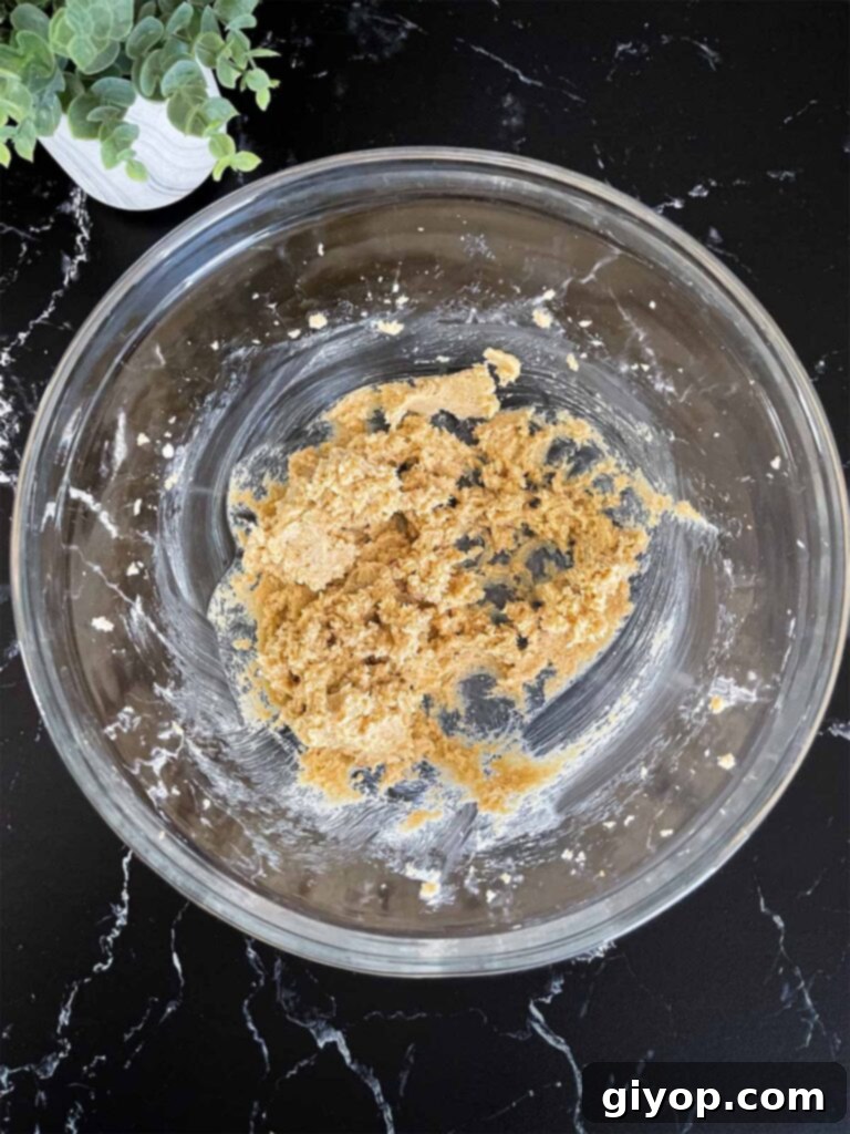 Unsalted butter, granulated sugar, and brown sugar being creamed together in a clear glass mixing bowl for Almond Joy cookies.