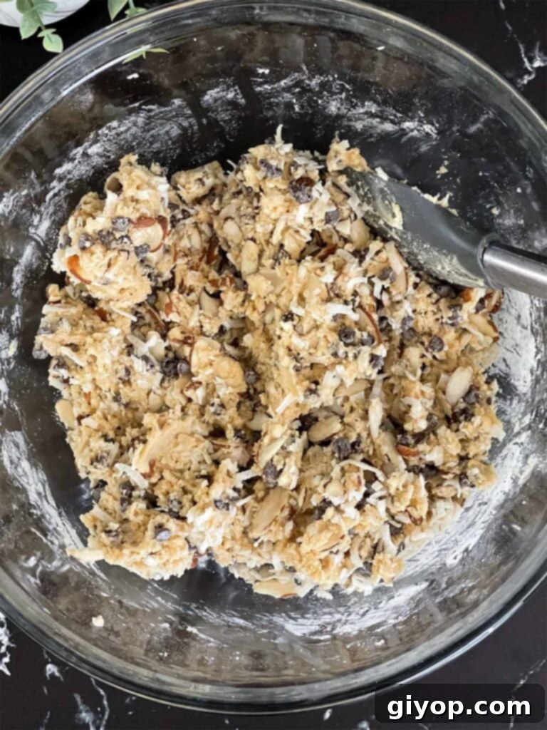 The finished Almond Joy cookie dough batter, rich with mini semi-sweet chocolate chips, shredded coconut flakes, and slivered almonds, ready for baking.
