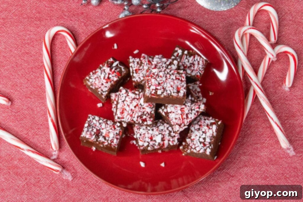 Decadent Easy Peppermint Fudge 5 Peppermint fudge on a red plate with scattered candy canes.