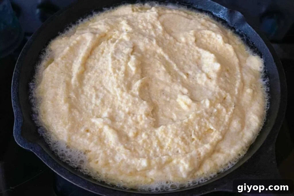 Sizzling cornbread batter poured into a hot cast iron skillet, indicating the start of a crispy crust formation.
