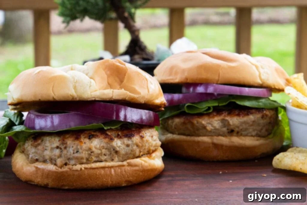 Two turkey burgers with lettuce and red onion on a cutting board.