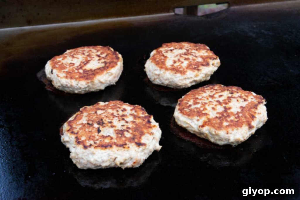 Four turkey burgers cooking on a flat top griddle