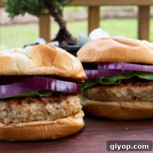 Two turkey burgers with lettuce and red onion on a cutting board.
