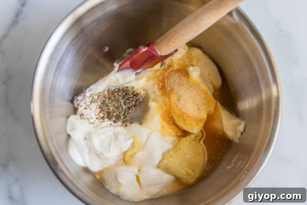 A metal bowl holds the creamy macaroni salad dressing ingredients, showcasing their smooth texture before mixing.