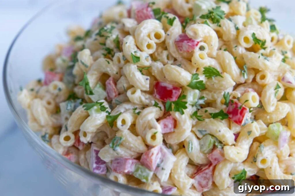 The finished creamy macaroni salad, garnished and ready for serving in an elegant glass bowl, reflecting its homemade freshness.
