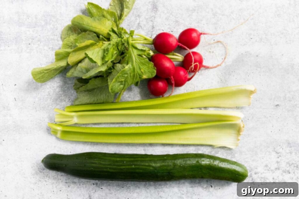 Freshly washed and prepared cucumber, radishes, and celery, ready for slicing, alongside fresh dill.