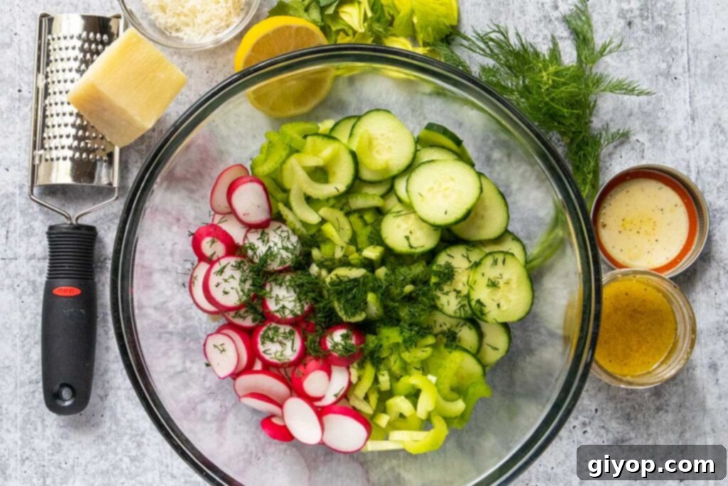 Sliced cucumbers, radishes, celery, and chopped fresh dill in a clear glass mixing bowl, ready for dressing.