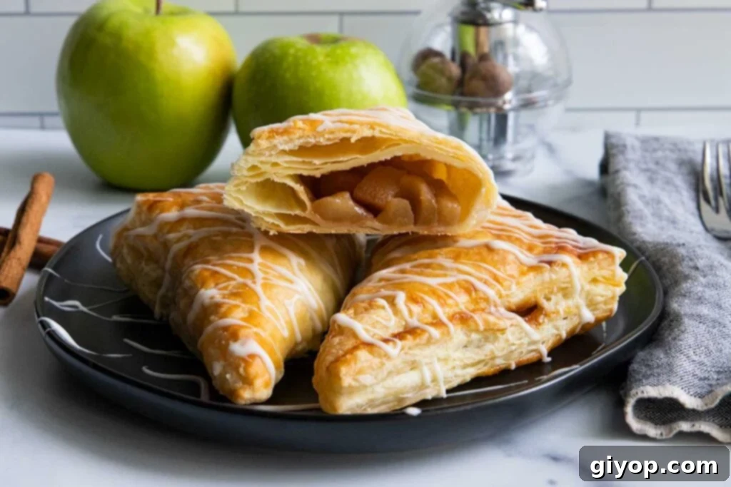 Apple turnovers on black plate with green apples in the background.