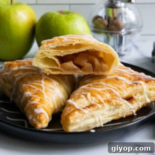 Apple turnovers on black plate with green apples in the background.