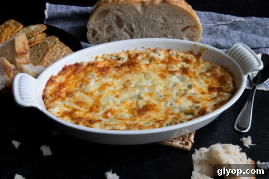 A delectable hot artichoke dip served in a white oval baking dish, with slices of crusty bread in the background, ready for dipping.