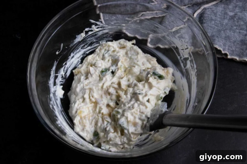 The creamy, unmixed base ingredients for artichoke dip—mayonnaise, sour cream, and cream cheese—in a clear glass mixing bowl, ready to be combined.