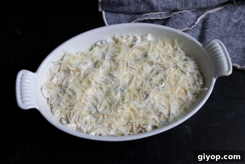 The prepared artichoke dip mixture, smooth and ready for baking, spread evenly in a white casserole dish before the final cheese topping.