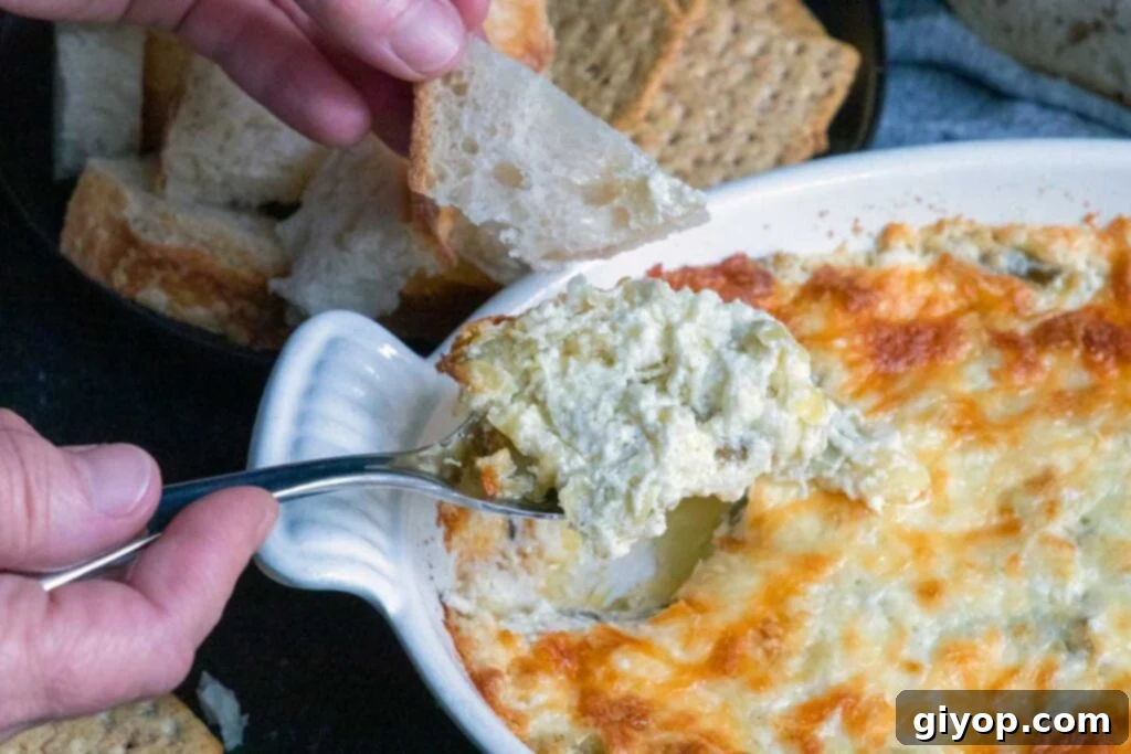 A serving spoon lifting a generous scoop of hot, gooey artichoke dip from the baking dish, highlighting its creamy and cheesy texture.