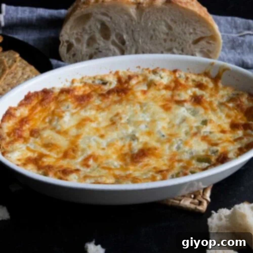 Artichoke dip in a white oval baking dish with bread in the background.