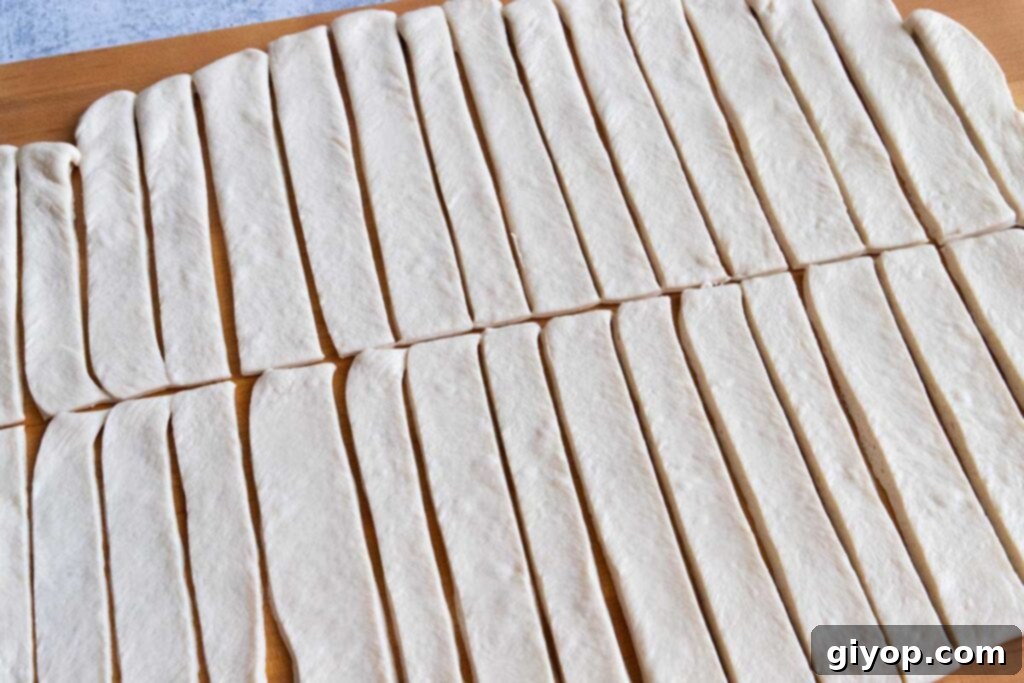 Pizza dough rolled out and cut into long strips on a wooden board.