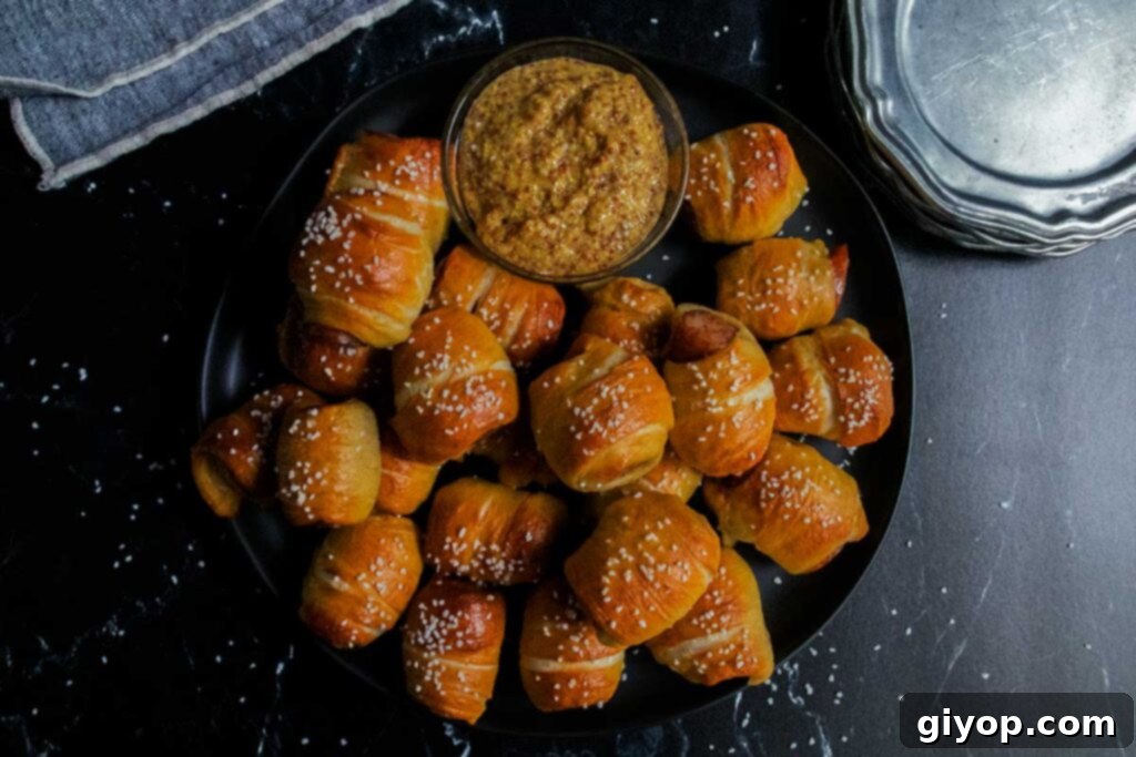 Close-up of sausage pretzel bites on a black plate, garnished with stone ground mustard.