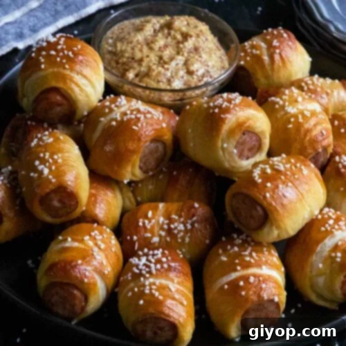Sausage pretzel bites with mustard on a black plate.