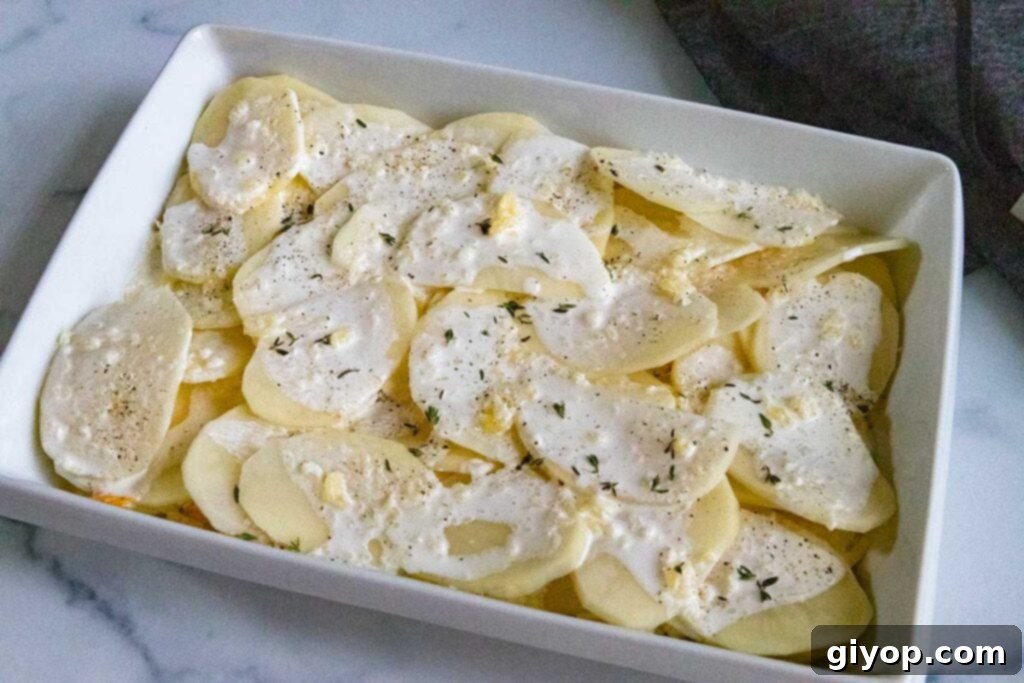 Sliced raw potatoes with cream sauce on top in a baking dish.