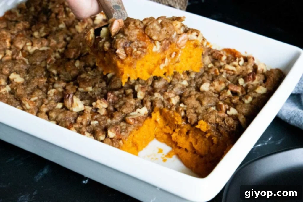 A perfectly golden slice of sweet potato casserole being served from a white baking dish.