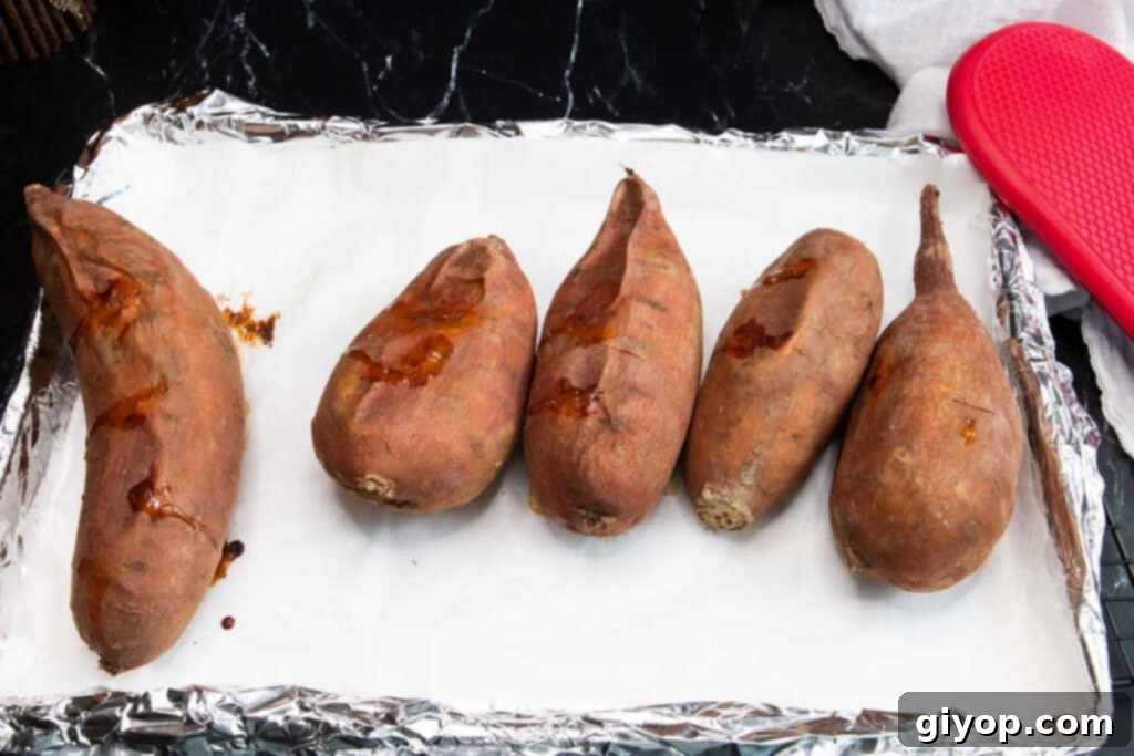 Baked sweet potatoes resting on a parchment-lined baking sheet.