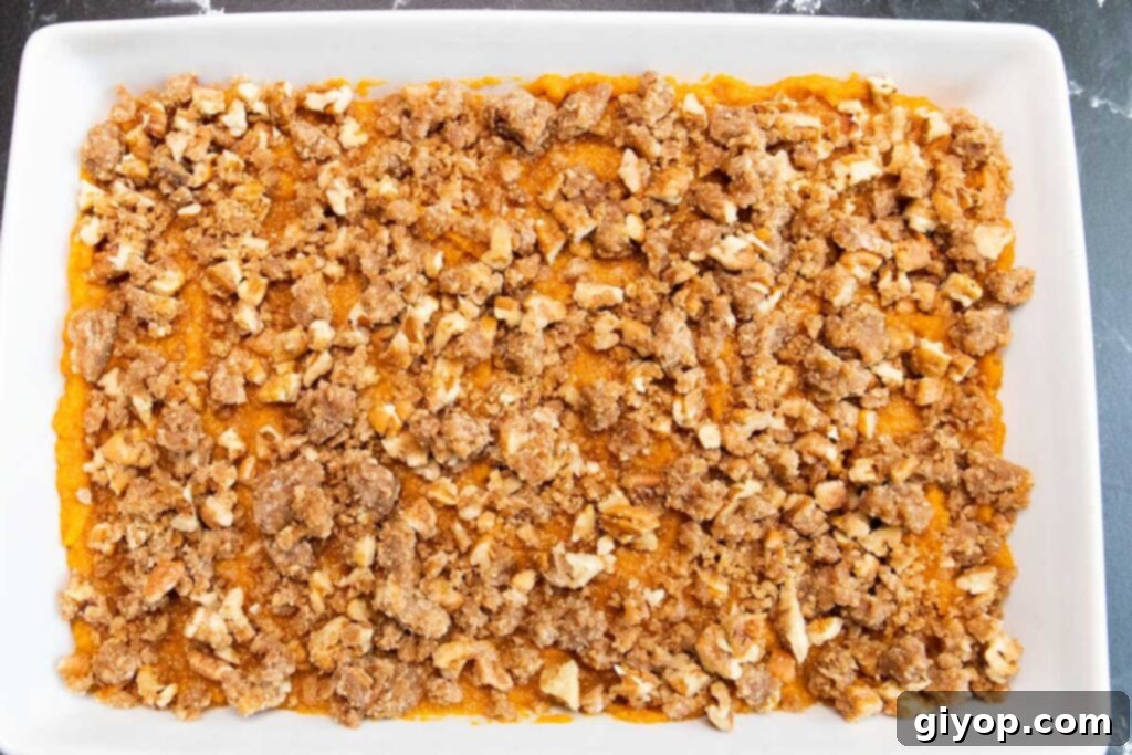 An unbaked sweet potato casserole in a white baking dish, topped with a pecan crumble.