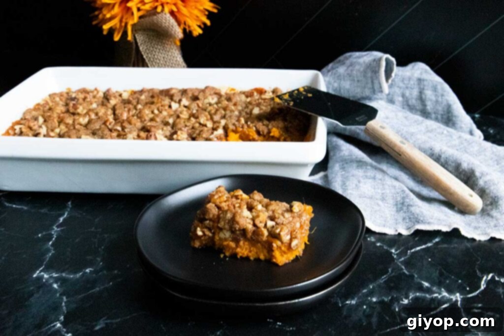 A generous serving of sweet potato casserole with pecan topping on a black plate.