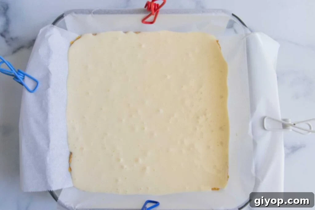 A smooth, creamy cheesecake layer has been poured over the baked graham cracker crust in the baking pan, ready for the pumpkin layer.