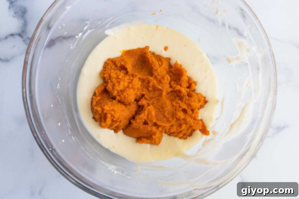 The pumpkin-infused cheesecake batter, rich in color and texture, is shown in a clear glass bowl, showcasing its readiness for layering.