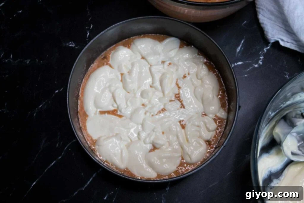 Cheesecake batter being dolloped over the carrot cake layer.