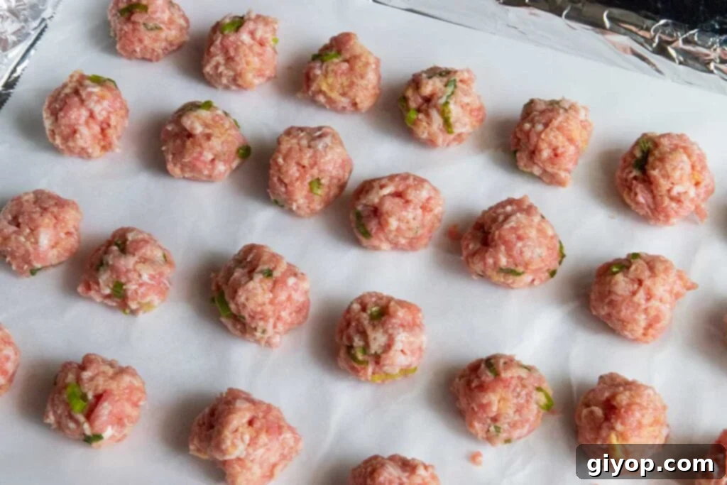 Raw, perfectly formed ground pork meatballs arranged on a parchment-lined baking sheet, ready for baking.