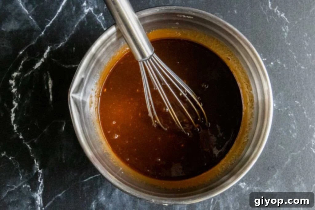 A vibrant Asian meatball sauce in a small mixing bowl, featuring hoisin, chili-garlic, soy, and sesame oil, ready to be heated.