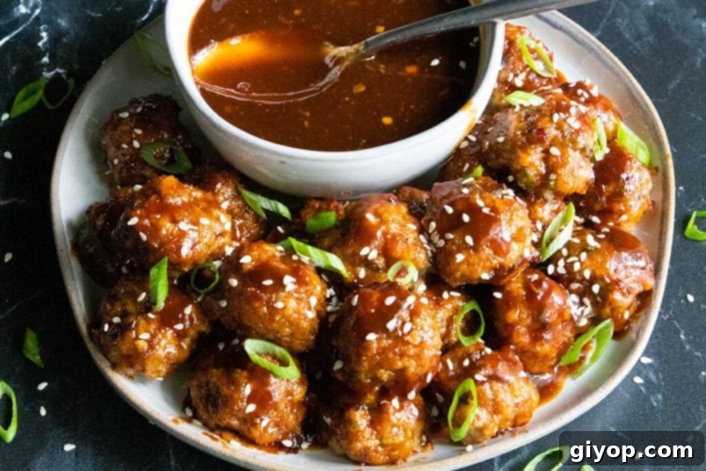 Platter of sticky, sweet and spicy Asian meatballs, garnished with green onions and sesame seeds, with extra dipping sauce on the side.