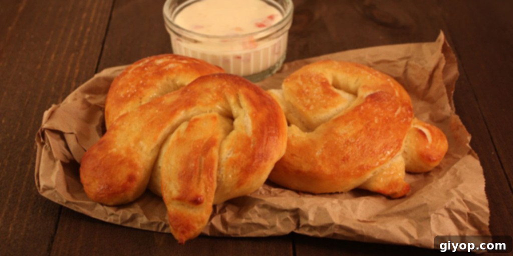 Freshly baked soft pretzels artfully arranged on brown parchment paper, accompanied by a small ramekin of golden cheese dip, highlighting their golden-brown crust and soft texture.