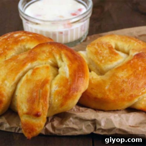 A freshly baked soft pretzel knot, golden brown and glistening with salt, resting on brown parchment paper.