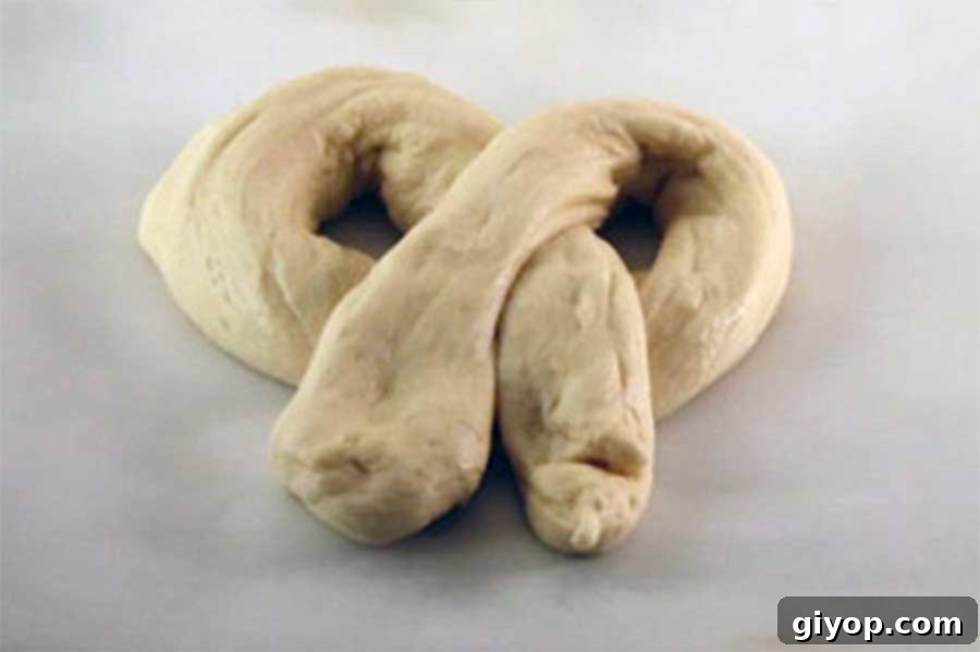 Several classic knot-shaped pretzel dough pieces arranged neatly on parchment paper, awaiting their baking soda bath and baking.