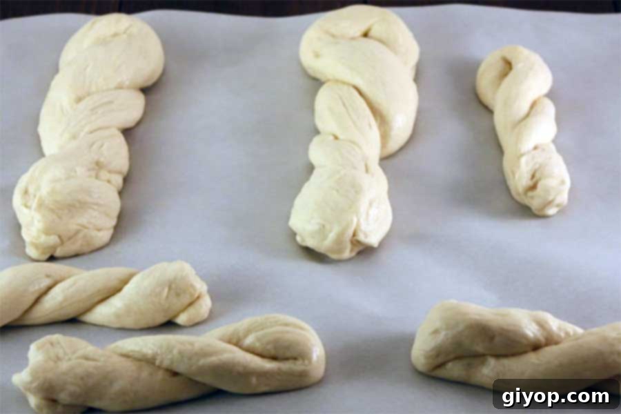 An array of various shaped pretzel dough, including classic knots and simple twisted sticks, displayed on parchment paper before baking.