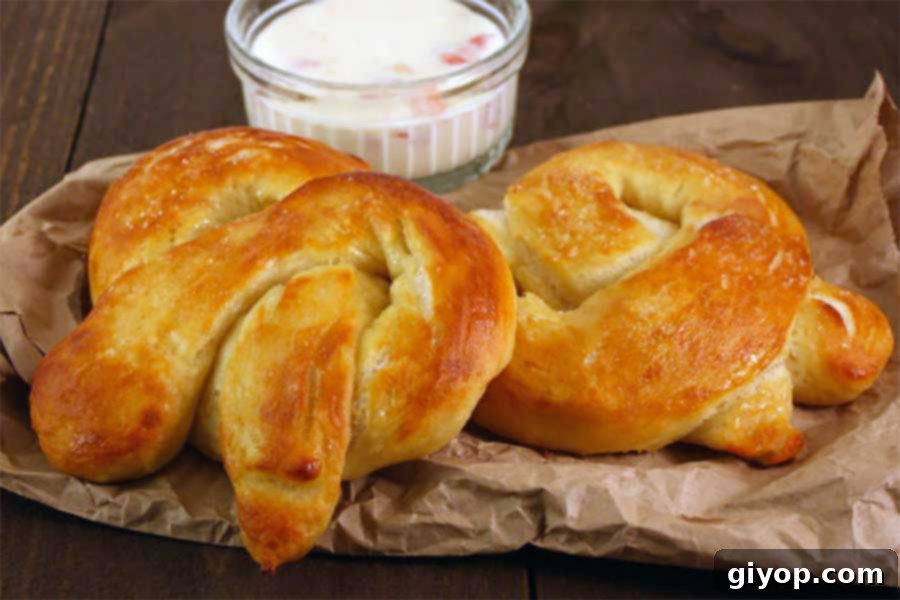 Golden-brown soft pretzels on brown paper with a ramekin of savory cheese dip in the soft-focus background, ready to be enjoyed.