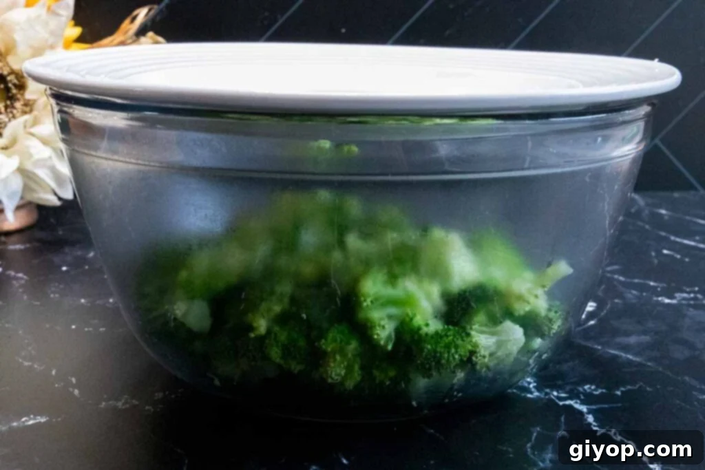 Fresh broccoli in a glass bowl with a plate on top as a lid, ready for blanching.