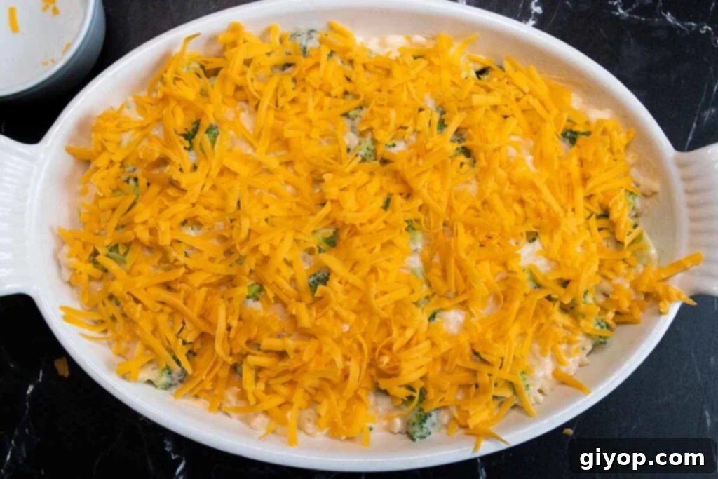 Unbaked casserole in a dish, generously topped with shredded cheddar cheese.