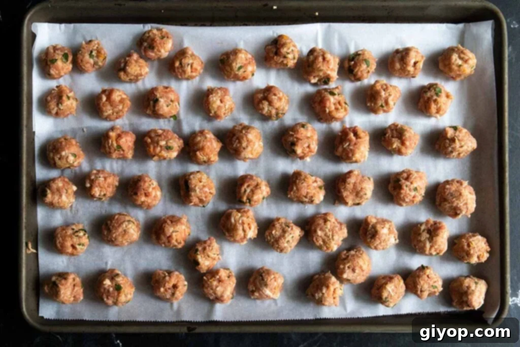 Tiny meatballs on a parchment lined baking sheet.