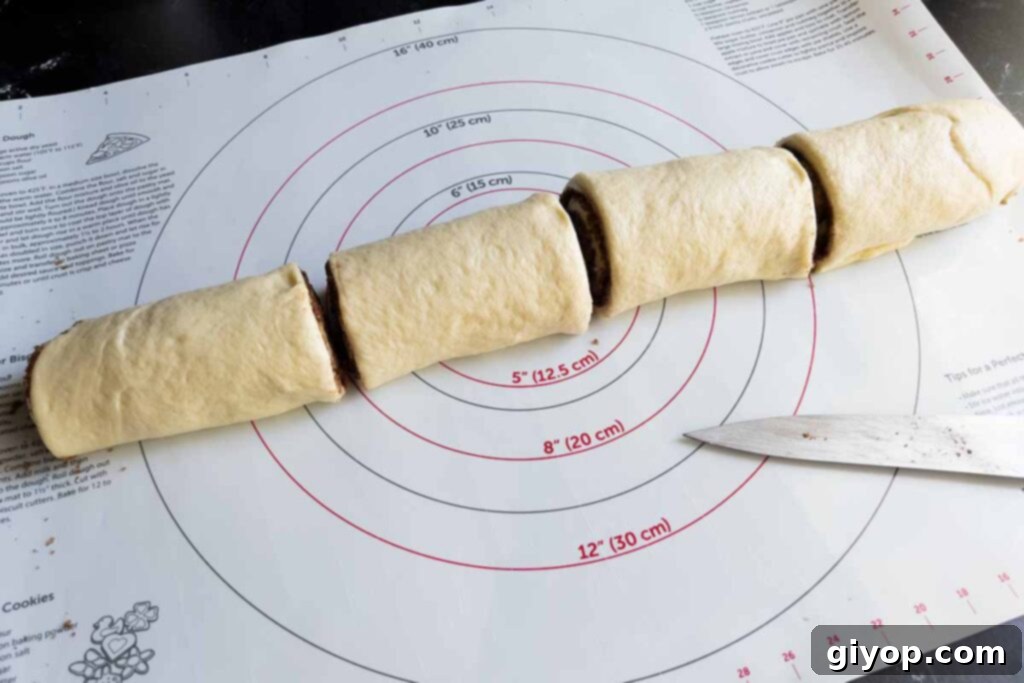 The initial cuts made to a long cinnamon roll dough log, dividing it into sections.