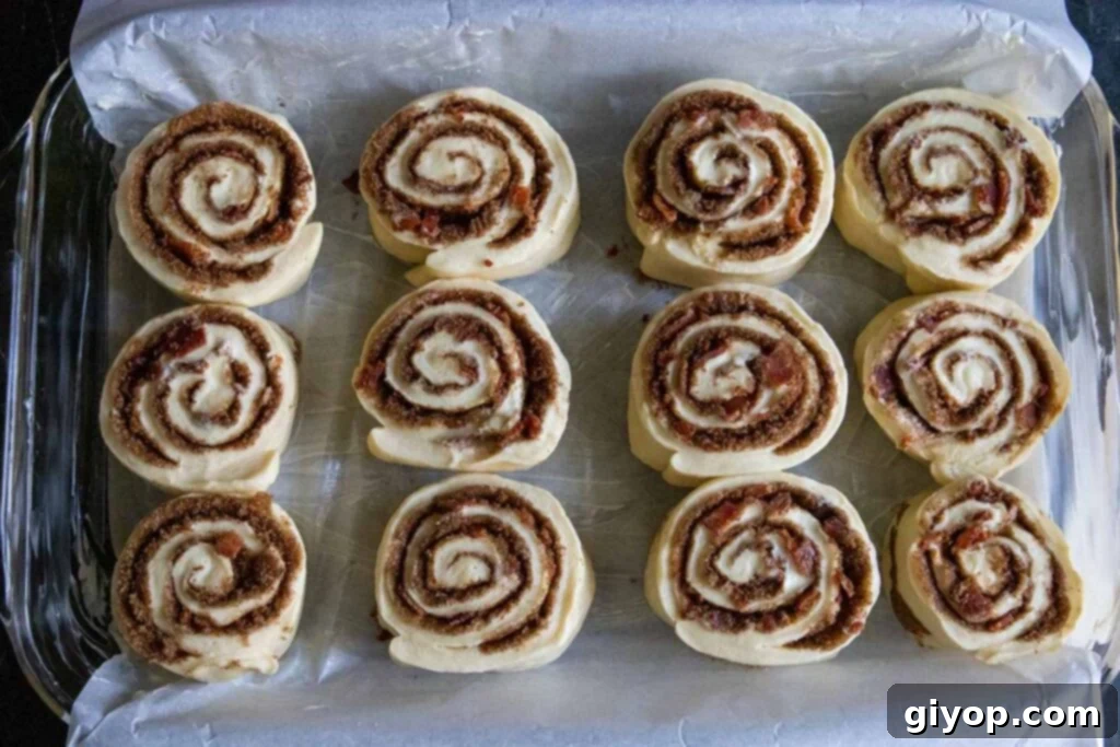 Unproofed maple bacon cinnamon rolls neatly arranged in a parchment paper-lined baking dish, spaced evenly.