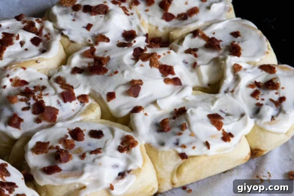 Maple bacon cinnamon rolls, generously iced and topped with extra crispy bacon, ready for serving.